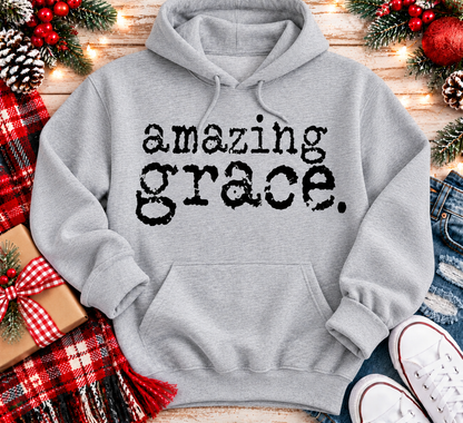A light gray pullover hoodie with the words 'amazing grace.' printed in a black typewriter-style font across the chest.