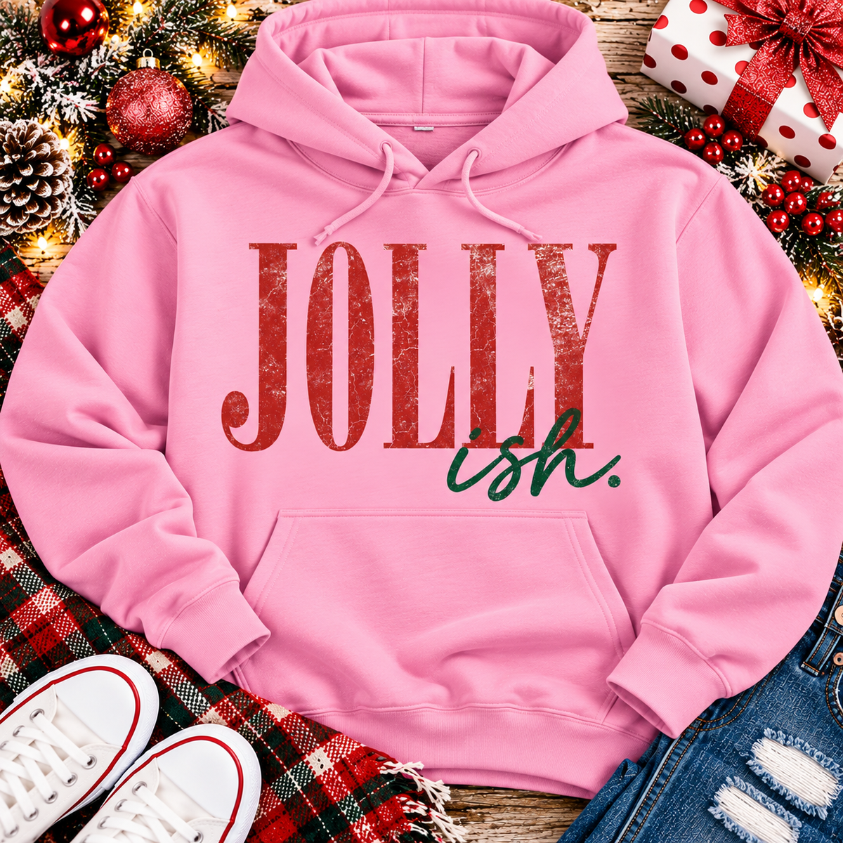 Jolly Ish Christmas graphic shirt featuring large distressed red JOLLY lettering with green handwritten ish script. Funny vintage-inspired holiday apparel available in pink and black, offered in short sleeve crewneck, V-neck, long sleeve and hoodie styles.