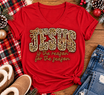 Jesus Is the Reason for the Season Christmas graphic shirt featuring bold leopard print JESUS lettering, decorative gold bows, and gold script. Faith-inspired holiday apparel available in red and black with four style options.
