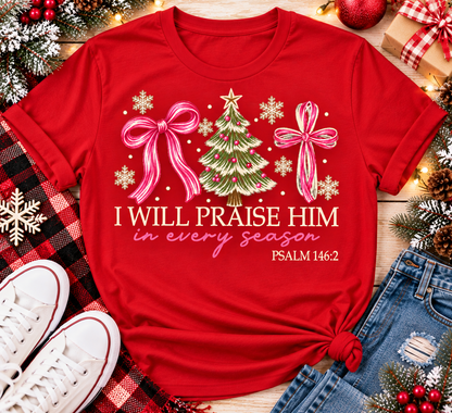 Christian Christmas shirt featuring I Will Praise Him in Every Season Psalm 146:2 graphic with pink bows, decorated Christmas tree, and cream snowflakes.