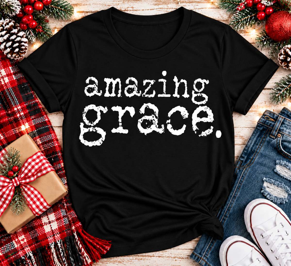 A black short-sleeve graphic T-shirt laid flat on a rustic wood surface, printed with the phrase 'amazing grace.' in distressed white lettering.