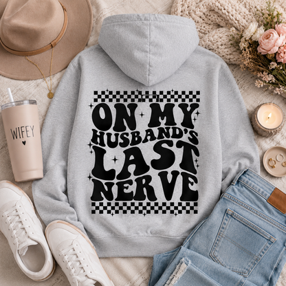 Gray graphic hoodie featuring bold black “On My Husband’s Last Nerve” lettering with checkerboard and sparkle details on the back.